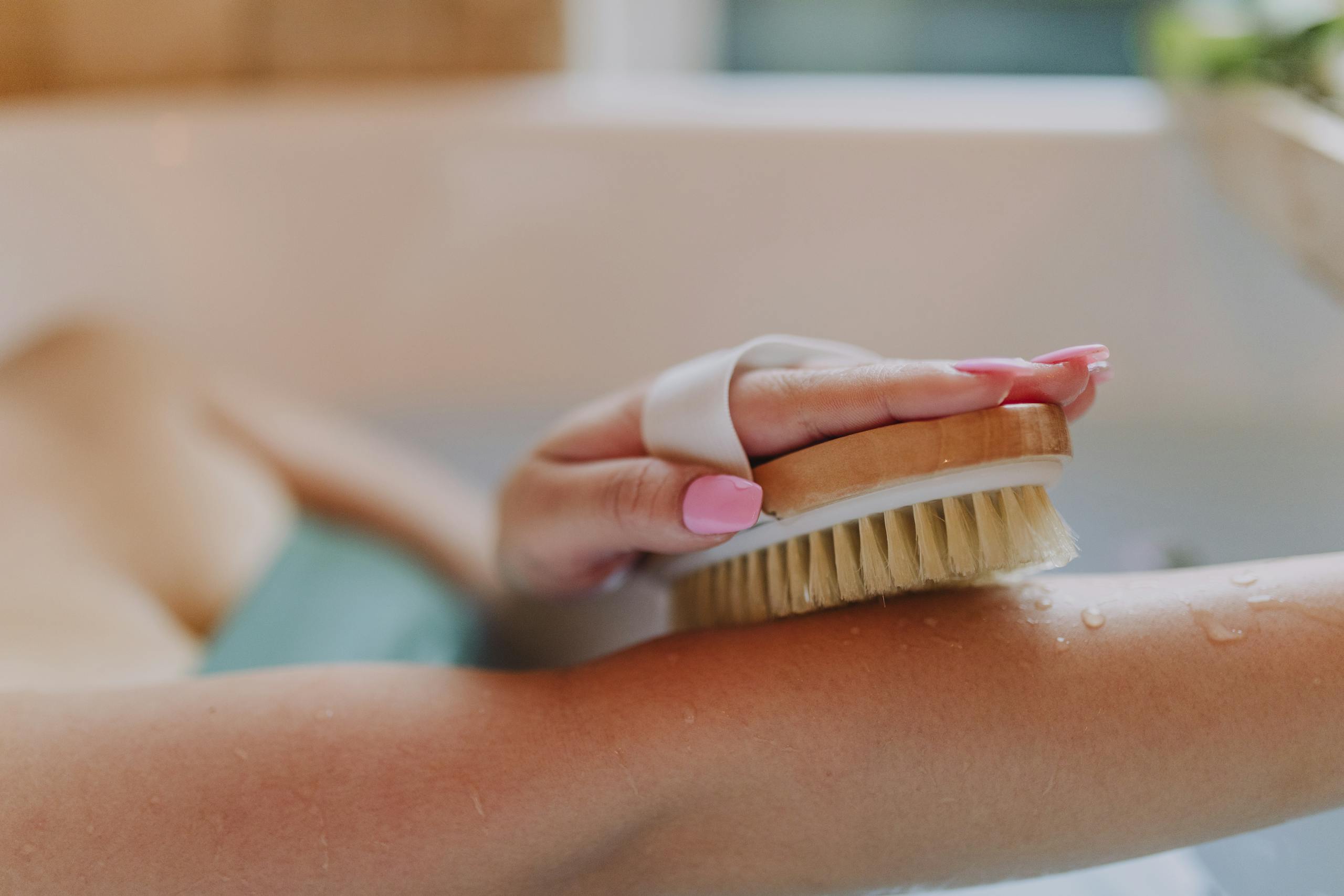Close-up of a hand using a dry brush on an arm in a relaxing bath setting.